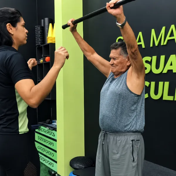 Aluno idoso fazendo exercício com bastão acompanhado por instrutora